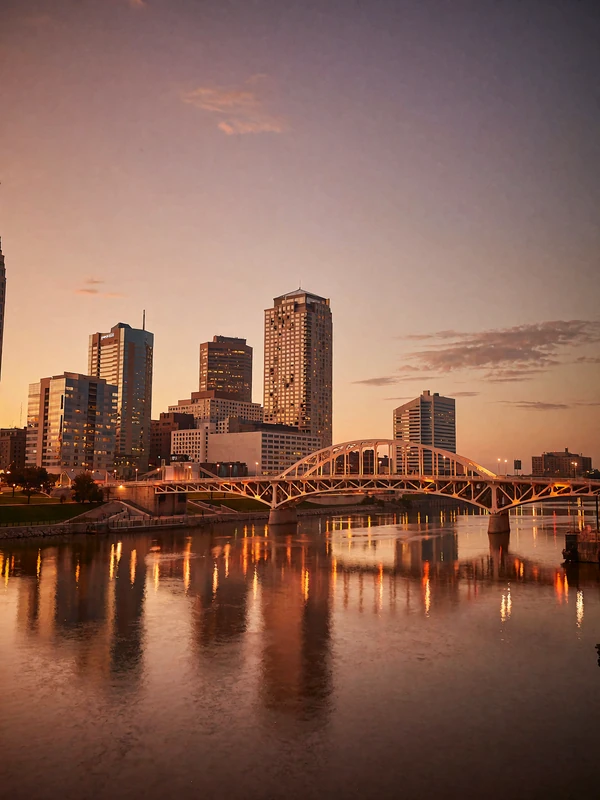Columbus riverfront skyline at dusk with an illuminated arched bridge and glass towers reflected in the water