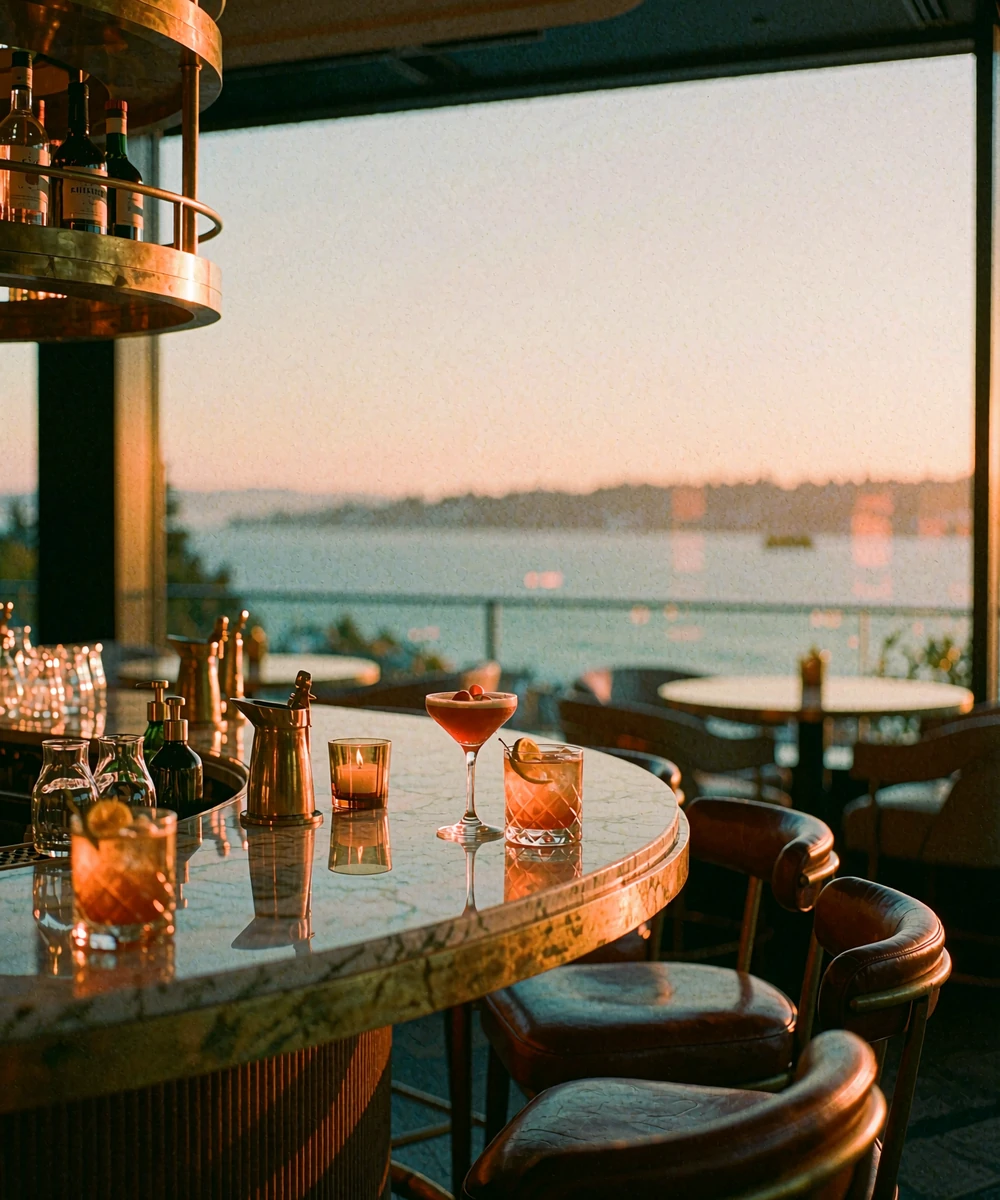 Marble bar-side table for two with amber cocktails beside a floor-to-ceiling window overlooking Elliott Bay at sunset