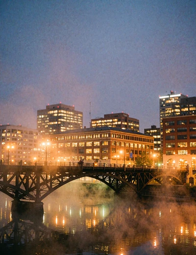 Portland riverfront at dusk with a steel bridge arcing over water reflecting warm city lights