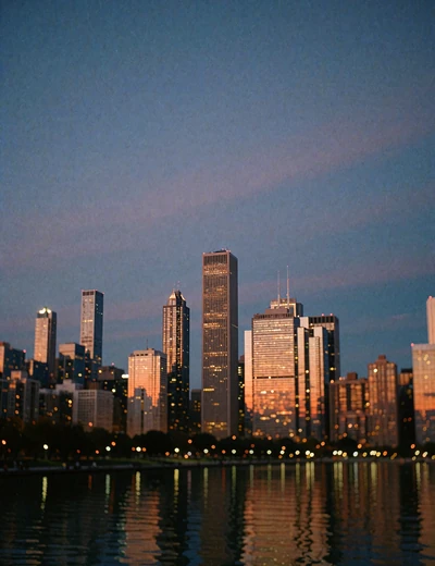 Chicago skyline glowing amber at blue hour above dark lake water