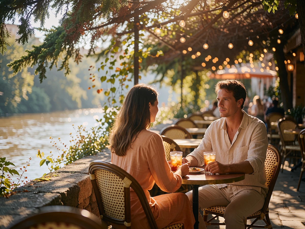 A young woman and a well-dressed man share drinks at a small table on a shaded San Antonio riverside terrace