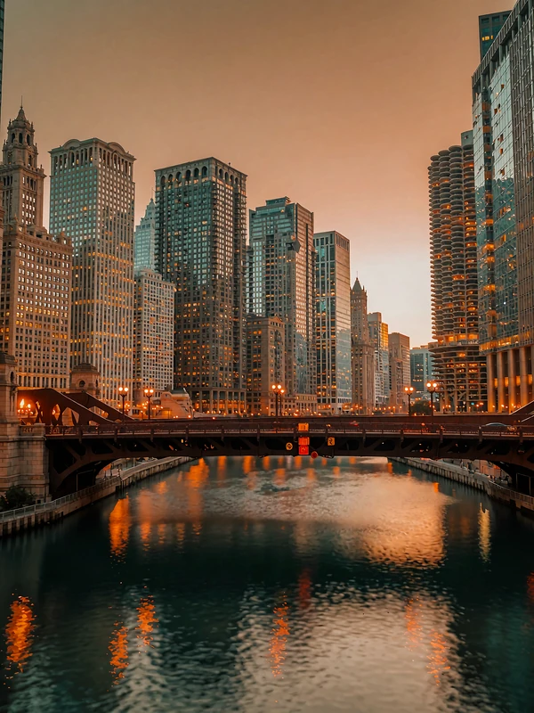 Chicago river corridor at dusk with tiered towers and warm window light reflected on dark water