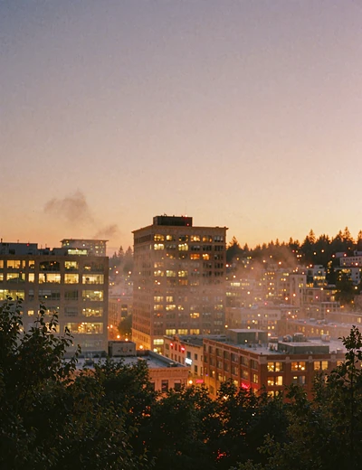 Downtown Portland skyline at early evening with warm window lights and a violet sky over tree canopy