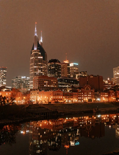 Nashville skyline at night reflected across the river with warm amber light